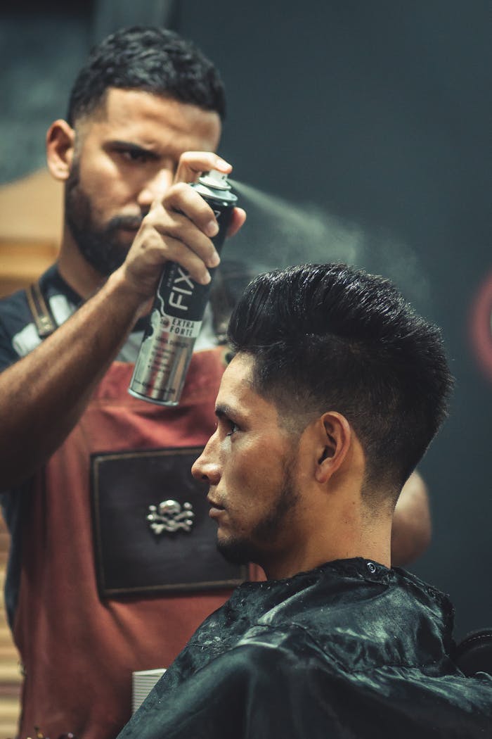 services-03 Experienced stylist applies finishing spray to clients hair during grooming session at modern barbershop.